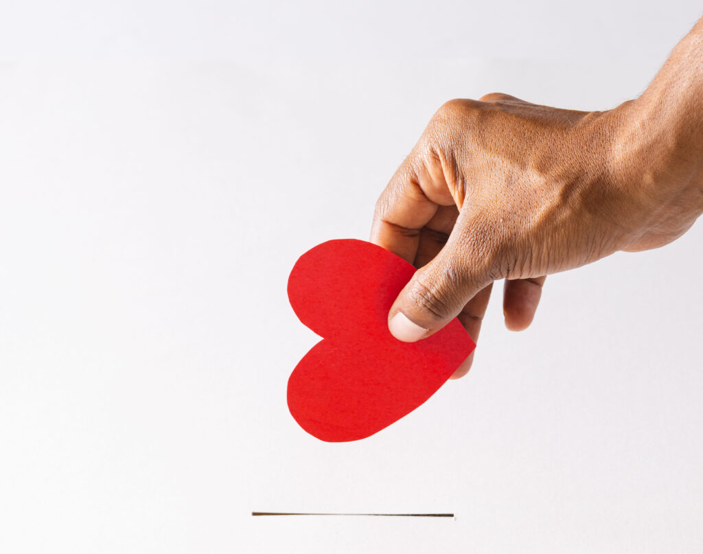 Hand of biracial man red heart into slot, on white background with copy space